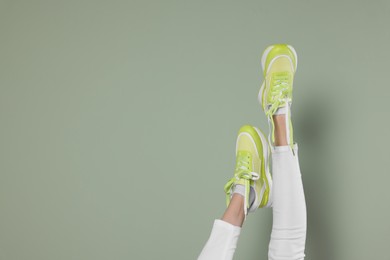 Photo of Woman wearing pair of new stylish sneakers on light green background, closeup. Space for text