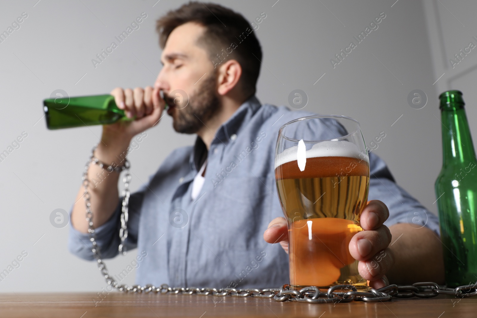 Photo of Addicted man chained to alcoholic drink at wooden table, focus on hand