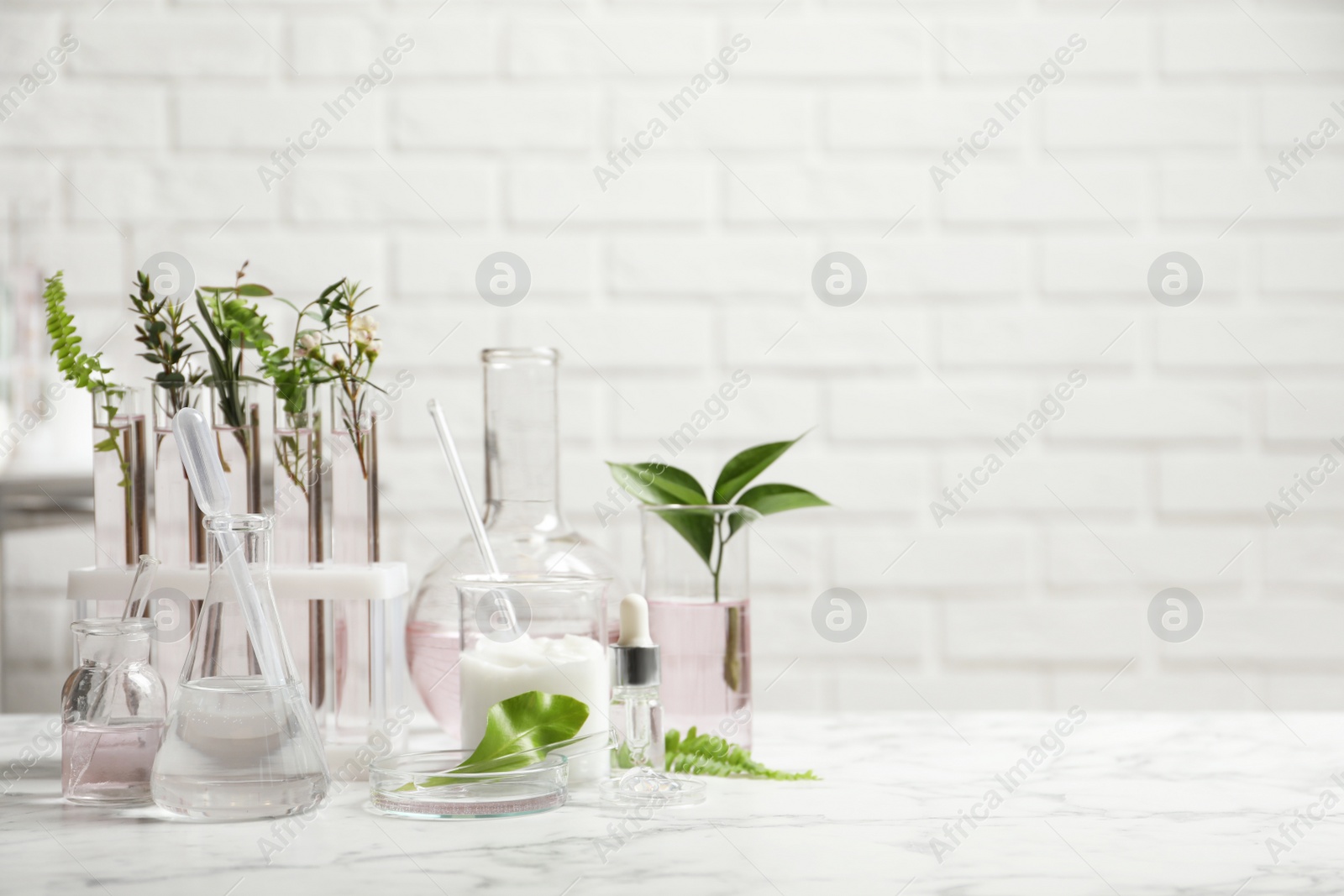 Photo of Organic cosmetic products, natural ingredients and laboratory glassware on white marble table, space for text