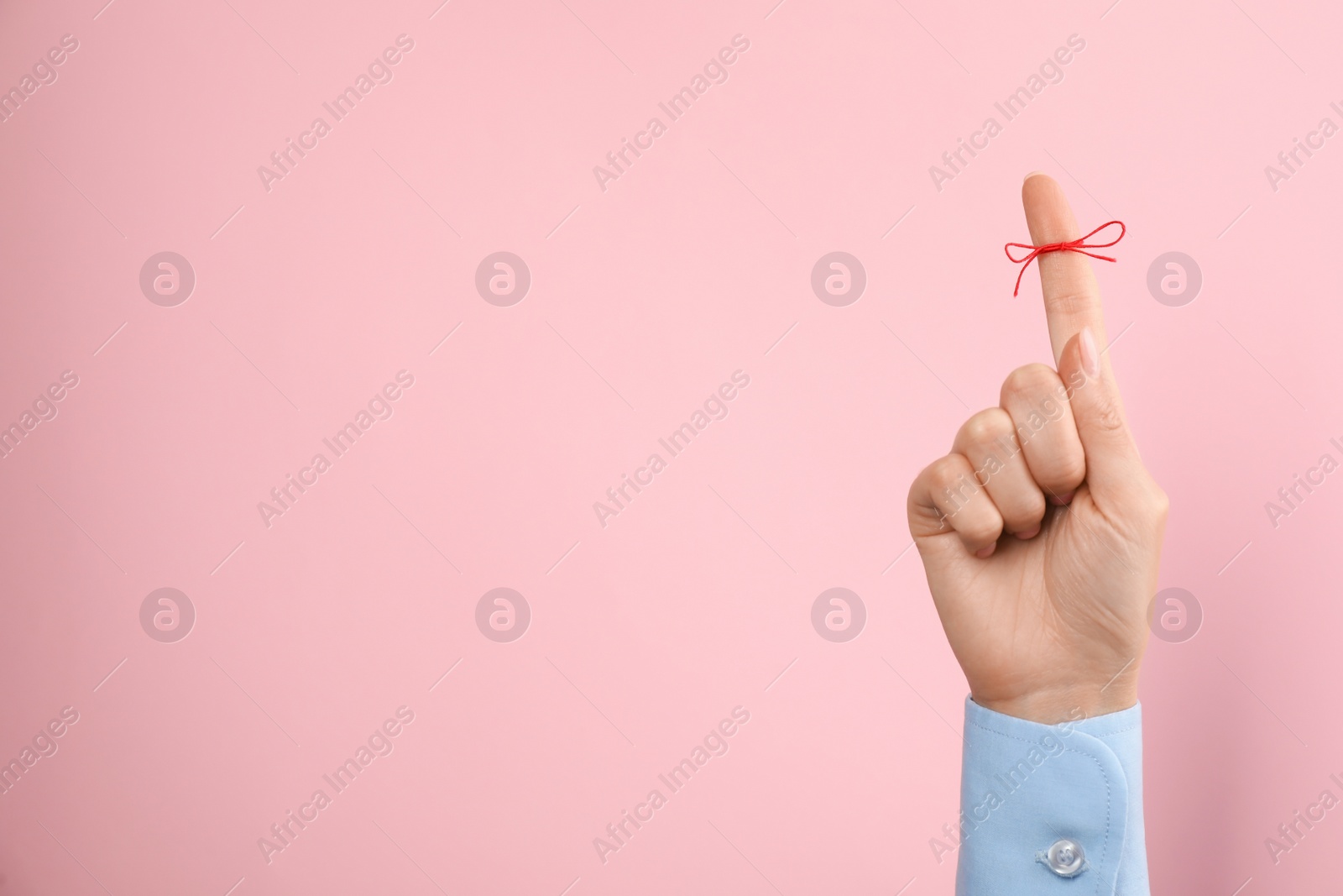 Photo of Woman showing index finger with tied red bow as reminder on pink background, closeup, Space for text