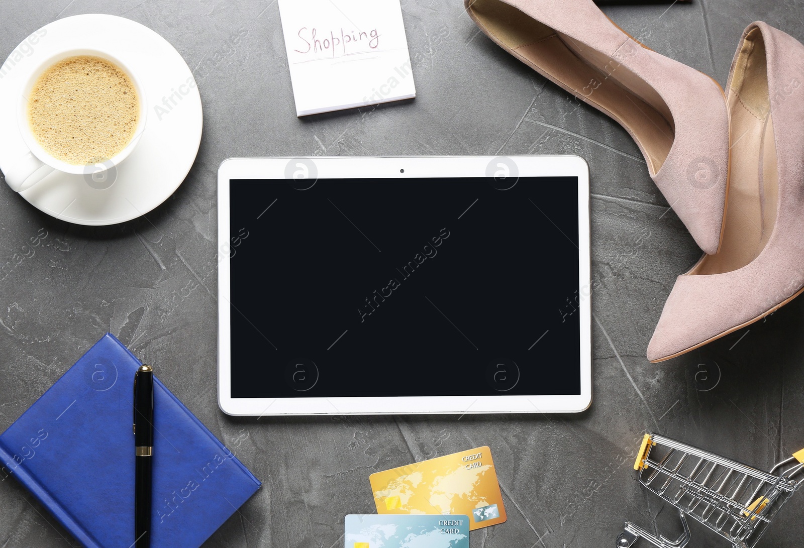 Photo of Online store. Tablet, stationery, shopping cart, credit cards, shoes and coffee on grey table, flat lay