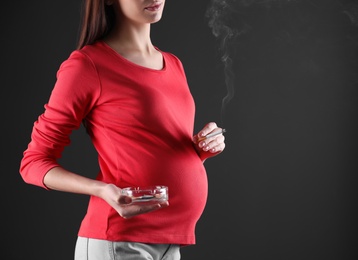 Photo of Pregnant woman smoking cigarette on black background, closeup. Space for text