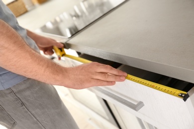 Man measuring kitchen furniture indoors, closeup. Construction tool