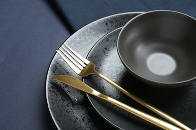 Stylish ceramic plates, bowl and cutlery on dark blue background, closeup