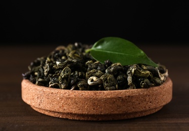 Photo of Dried green tea leaves in cork bowl on wooden table, closeup