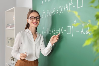 Photo of Young math’s teacher explaining mathematical equations near chalkboard in classroom