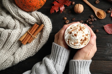 Woman holding cup with tasty pumpkin spice latte at black wooden table, top view