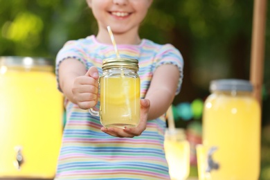 Photo of Little girl with natural lemonade in park, closeup. Summer refreshing drink