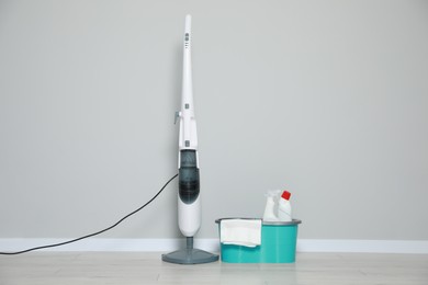 Photo of Modern steam mop and bucket with different cleaning supplies on floor near grey wall