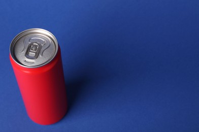 Energy drink in red can on blue background, space for text