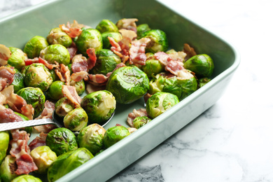 Photo of Delicious Brussels sprouts with bacon on white marble table, closeup
