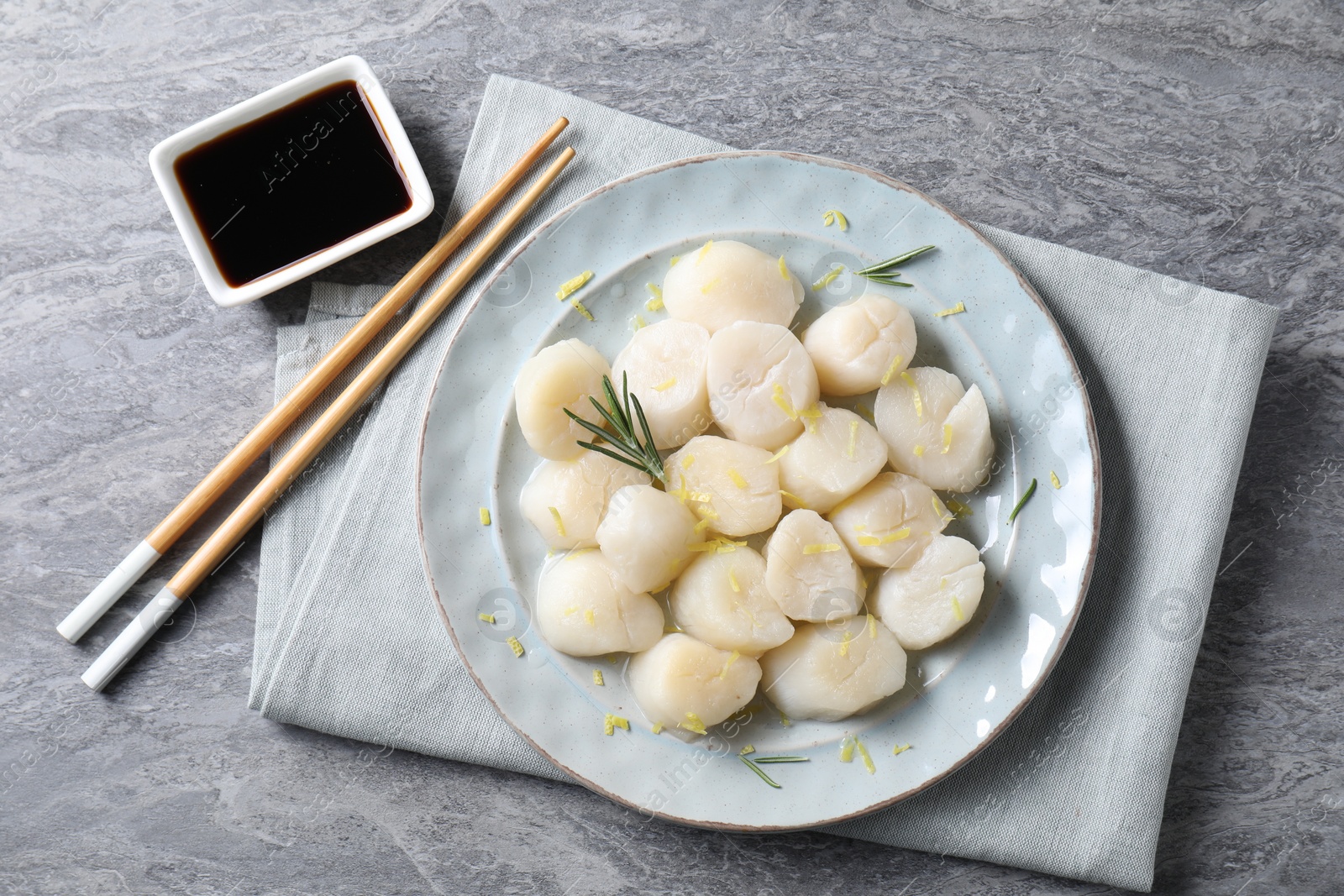 Photo of Raw scallops with lemon zest, rosemary and soy sauce on grey marble table, flat lay