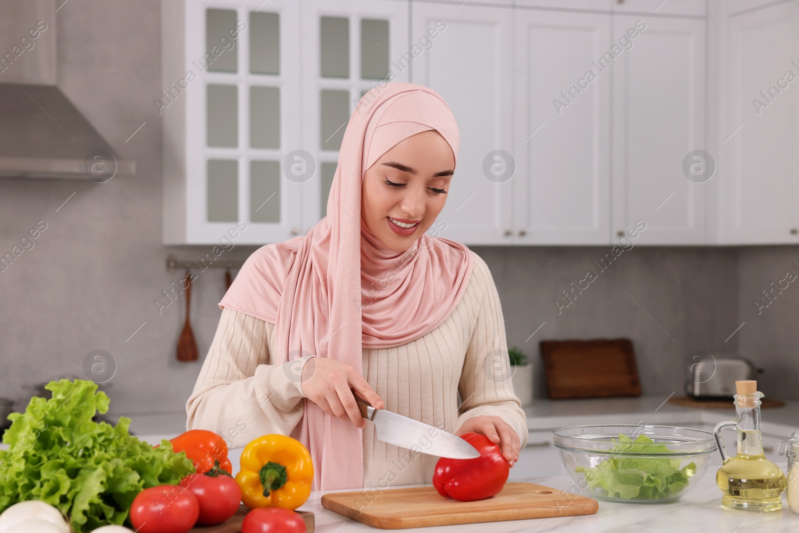 Photo of Muslim woman making delicious salad with vegetables at white table in kitchen