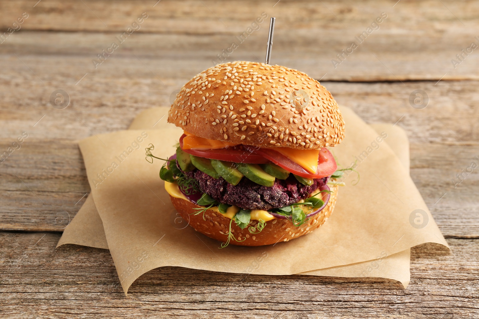 Photo of Tasty vegetarian burger with beet cutlet, cheese, avocado and tomato on wooden table