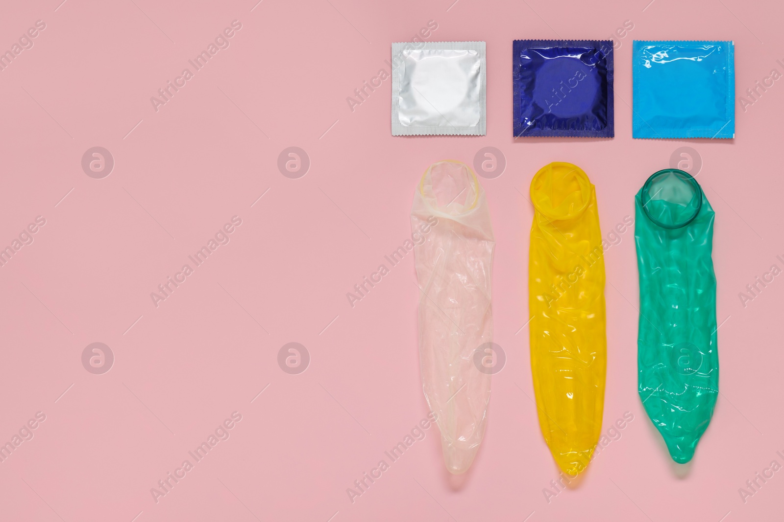 Photo of Unrolled condoms and packages on pink background, flat lay with space for text. Safe sex