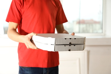 Young man with pizza boxes indoors, space for text. Food delivery service