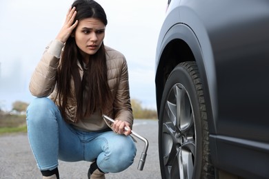 Photo of Worried young woman near car with punctured wheel on roadside