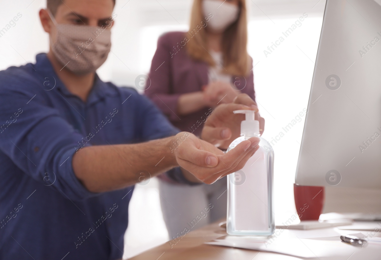 Photo of Office worker using sanitizer at table, focus on hands. Personal hygiene during COVID-19 pandemic