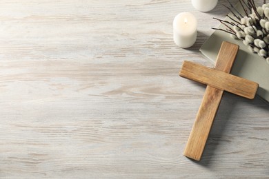 Photo of Burning candles, cross, book and willow branches on wooden table, flat lay. Space for text