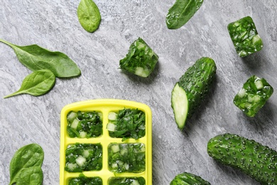 Flat lay composition with ice cube tray, spinach and cucumbers on table