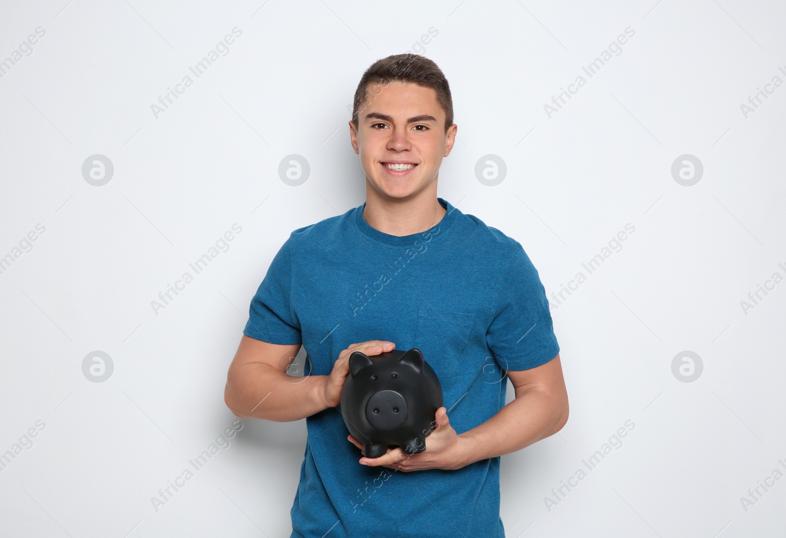 Photo of Teenage boy with piggy bank on white background