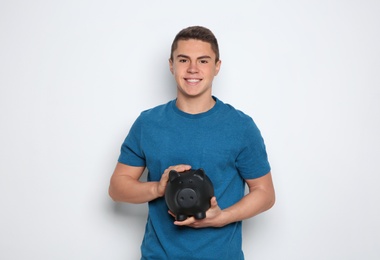 Teenage boy with piggy bank on white background