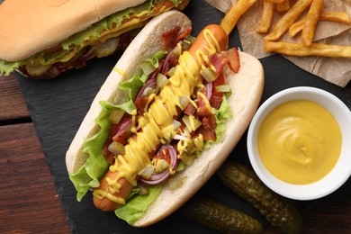 Photo of Delicious hot dogs with lettuce, onion and pickle served on wooden table, flat lay