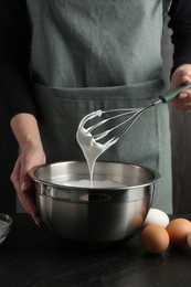 Photo of Woman making whipped cream with whisk at black table, closeup