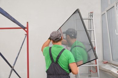 Photo of Worker in uniform holding double glazing window indoors, back view