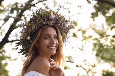 Photo of Young woman wearing wreath made of beautiful flowers outdoors on sunny day