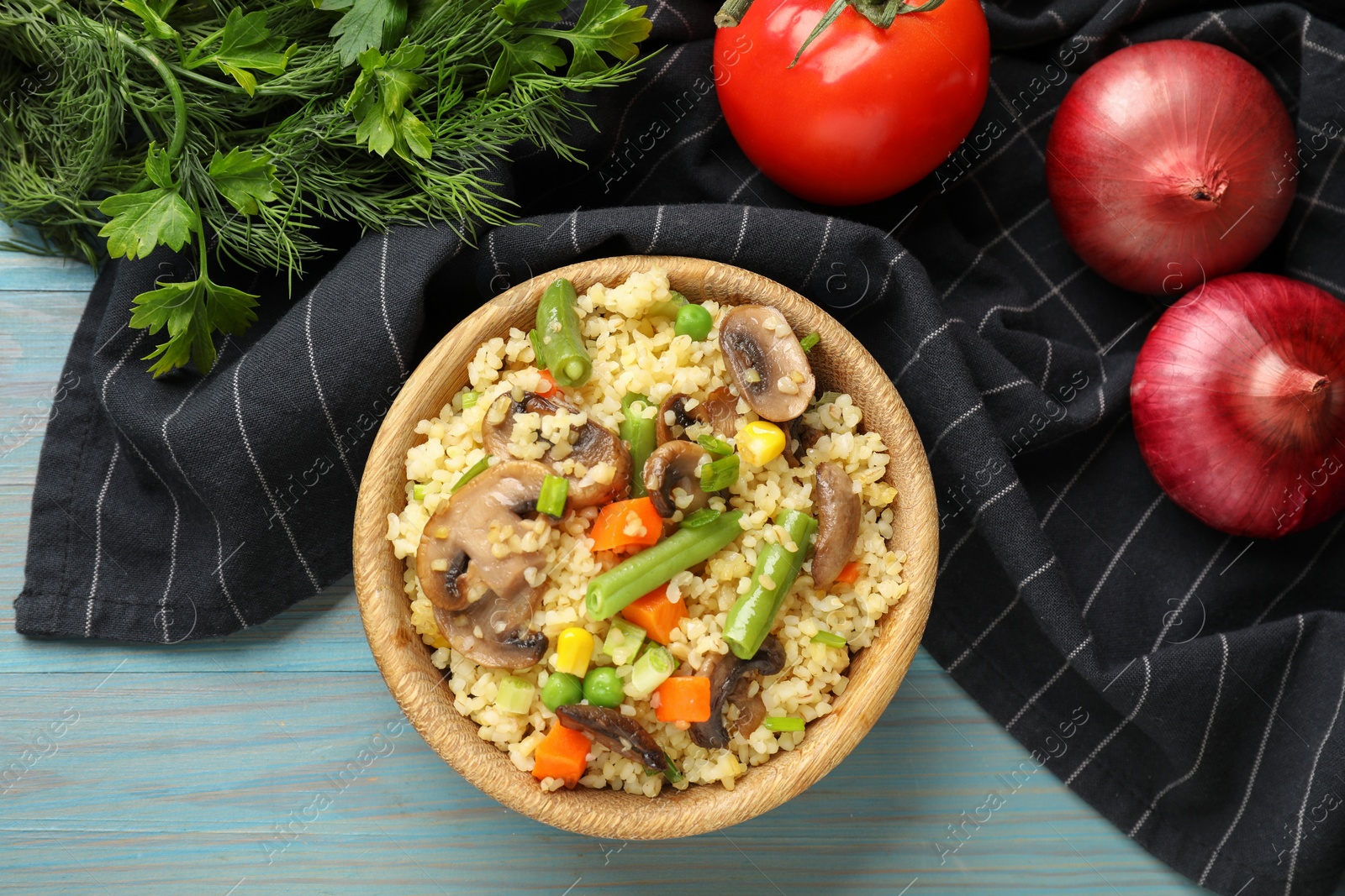 Photo of Delicious bulgur with vegetables, mushrooms and other products on light blue wooden table, top view