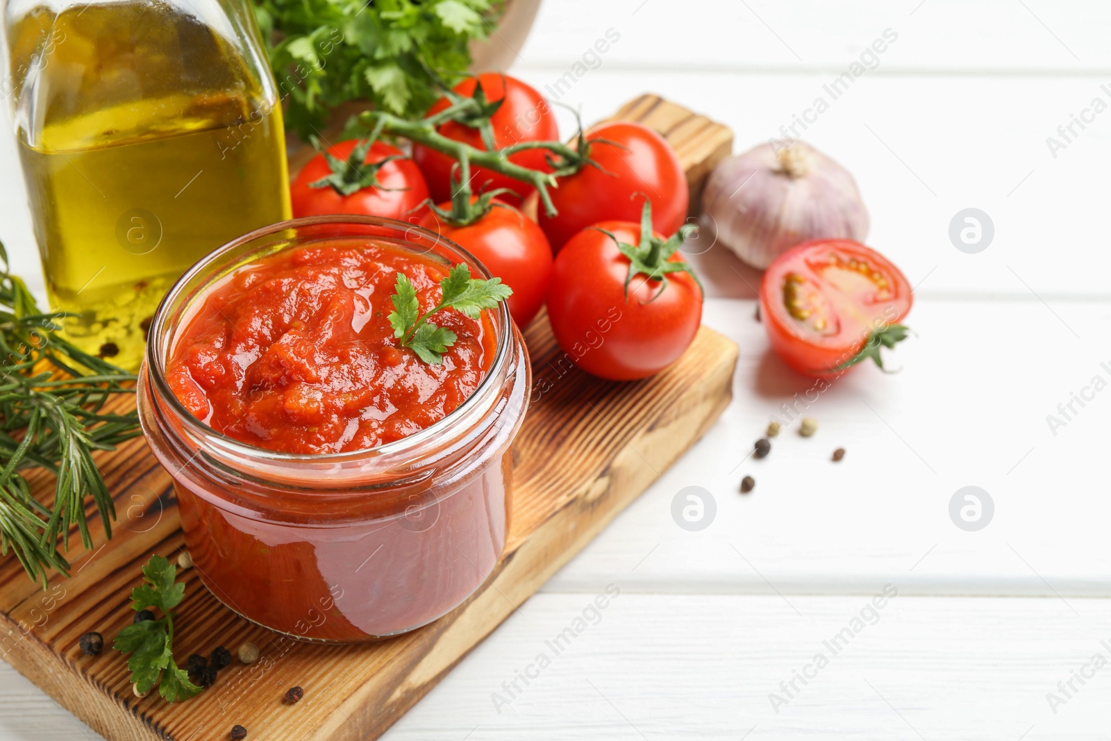 Photo of Homemade tomato sauce in jar and fresh ingredients on white wooden table, closeup