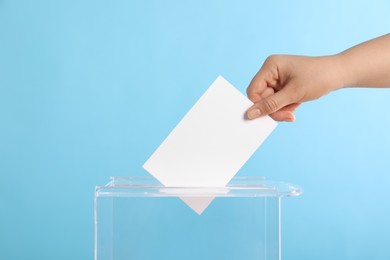 Woman putting her vote into ballot box on light blue background, closeup