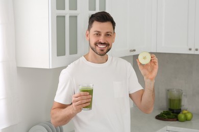 Photo of Happy man holding glass of delicious smoothie and apple slice in kitchen