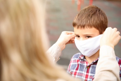 Mother putting mask onto face of little son on playground during covid-19 quarantine