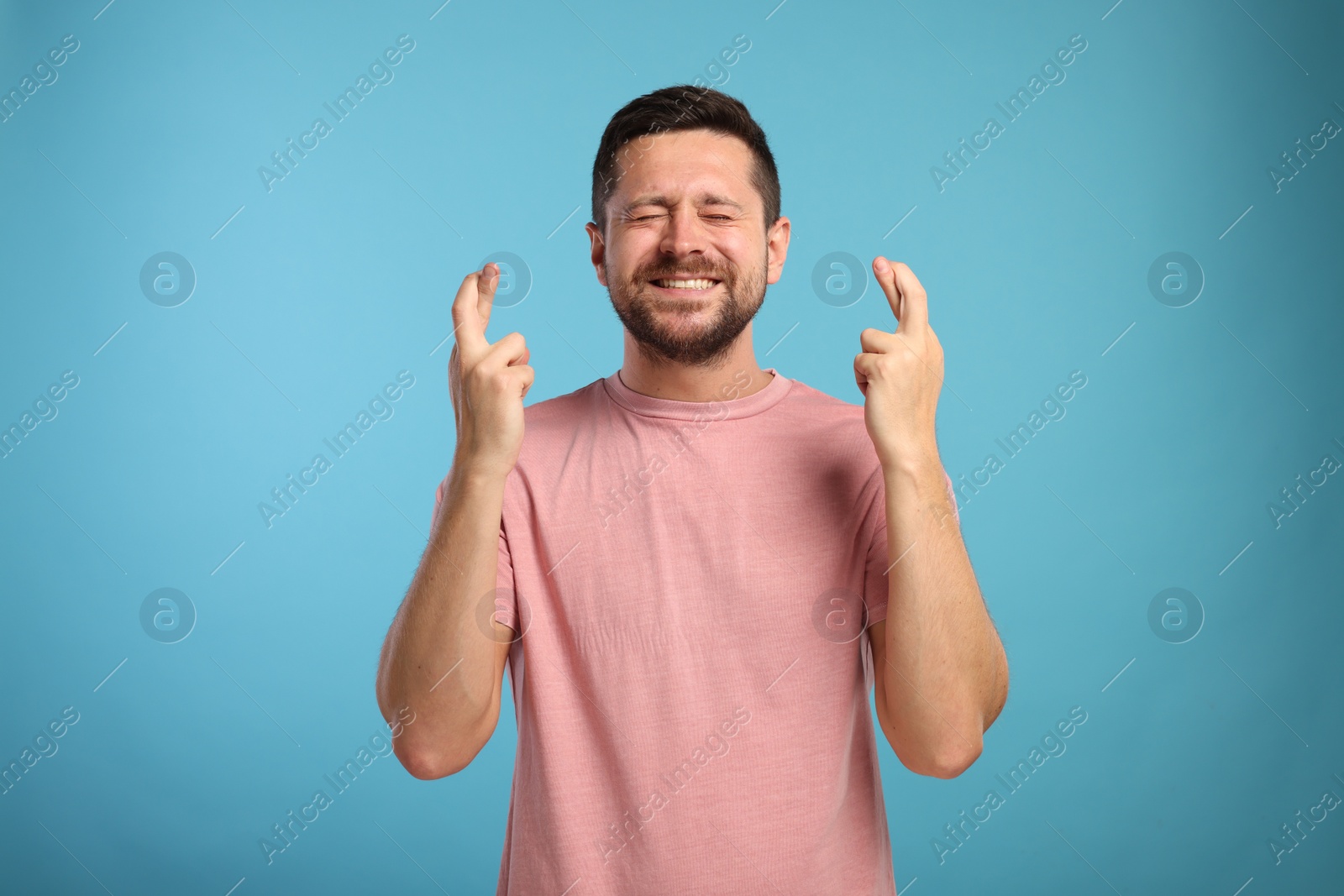 Photo of Emotional man crossing his fingers on light blue background