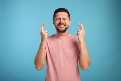 Emotional man crossing his fingers on light blue background