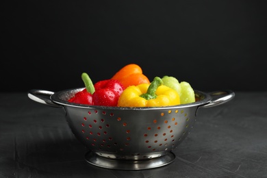 Colander with wet ripe bell peppers on grey table against black background