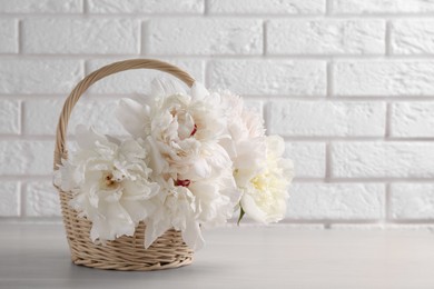 Photo of Beautiful peonies in wicker basket on white table near brick wall