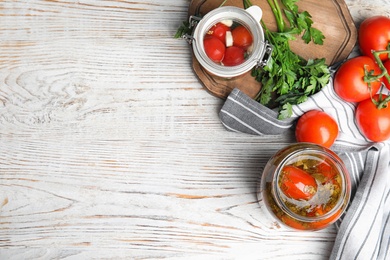 Photo of Flat lay composition with pickled tomatoes in glass jars on white wooden table, space for text