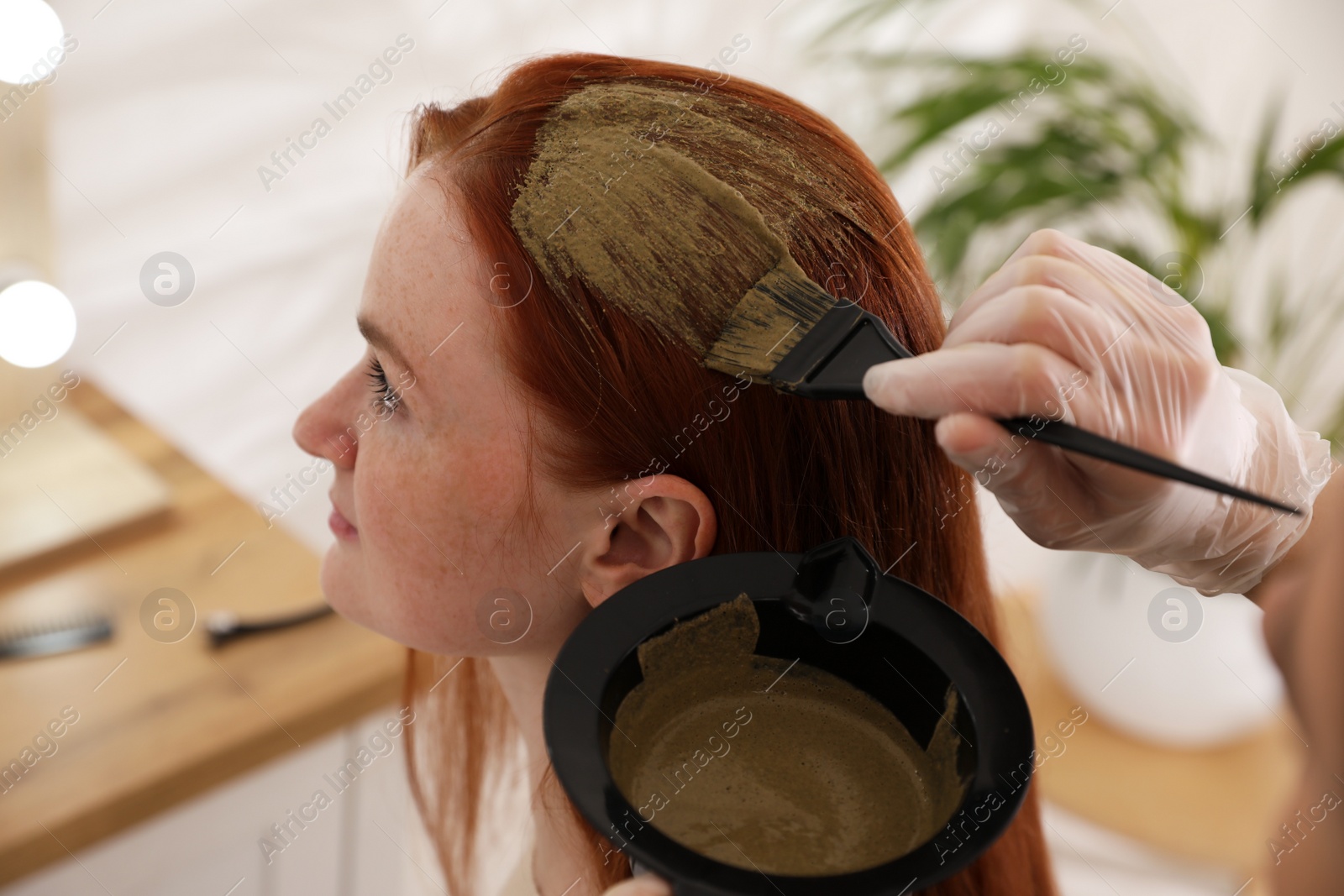 Photo of Professional hairdresser dyeing woman's hair with henna in beauty salon