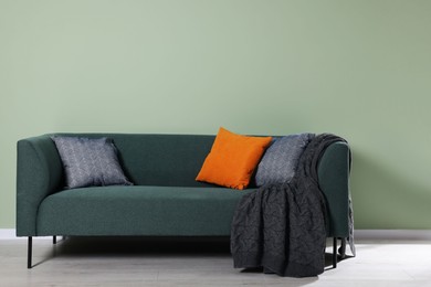 Comfortable sofa with decorative cushions and blanket indoors