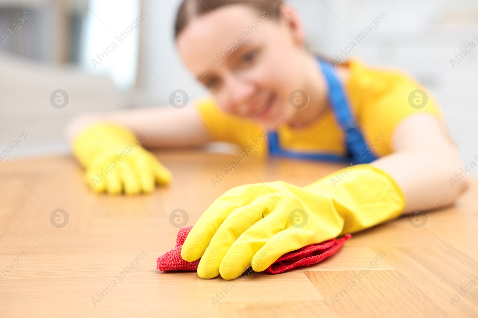 Photo of Woman cleaning wooden table with rag indoors, selective focus