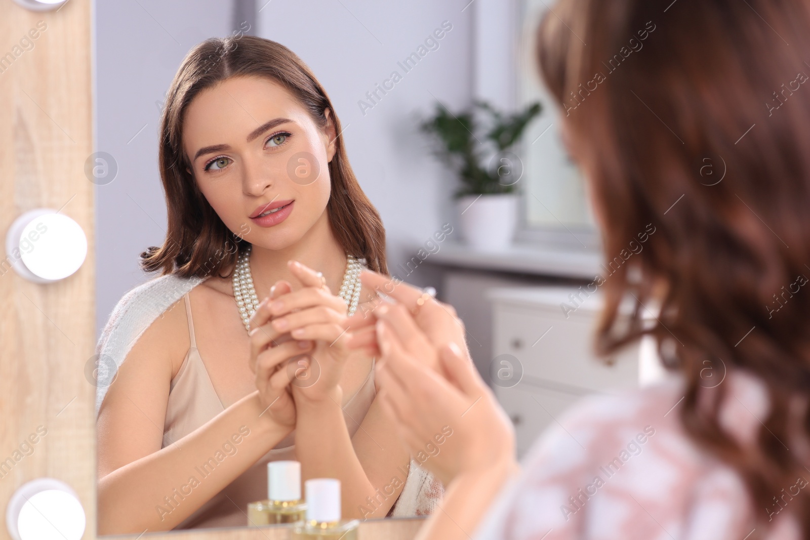 Photo of Young woman trying on elegant pearl jewelry at dressing table indoors