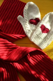 Photo of Red knitted scarf and mittens on yellow wooden table, top view