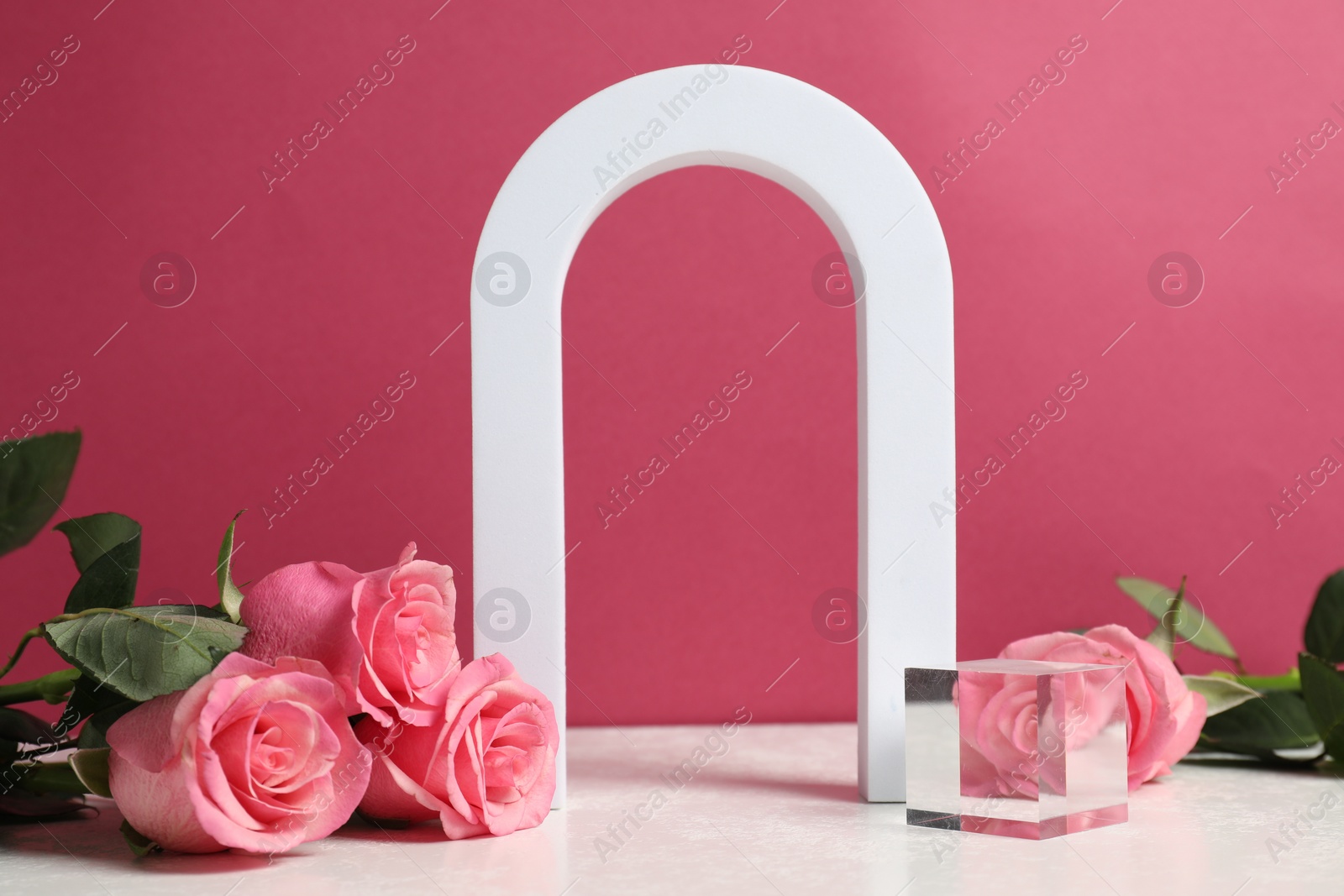 Photo of Stylish presentation for product. Geometric figures and beautiful roses on light table against pink background