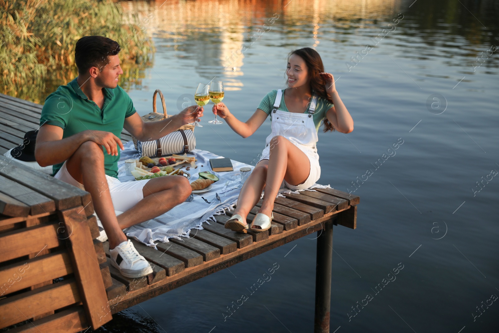 Photo of Couple clinking glasses with wine on pier at picnic