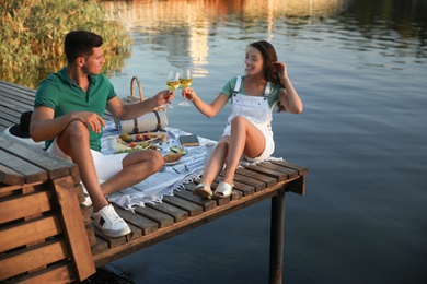 Couple clinking glasses with wine on pier at picnic