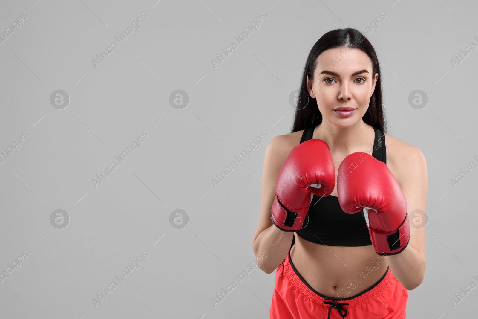 Photo of Portrait of beautiful woman in boxing gloves on grey background. Space for text