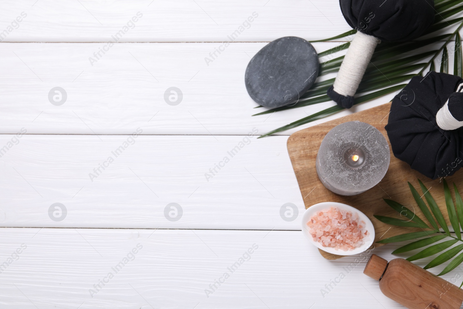 Photo of Beautiful spa composition with herbal massage bags, burning candle and leaves on white wooden table, flat lay. Space for text